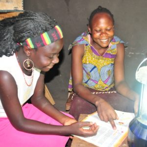 a few young women looking at a book while making use of a solar lantern